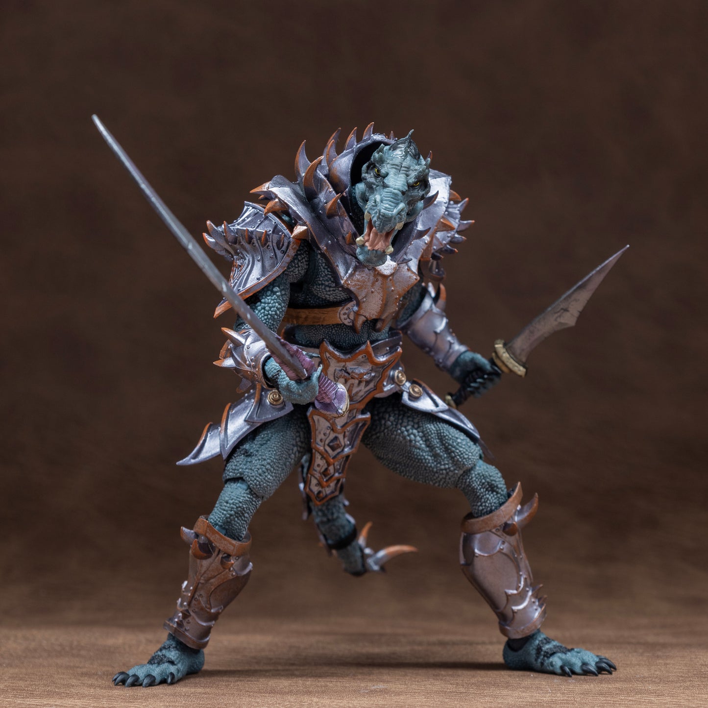 Fully armored green Saurian in a wide footed stance holding a scimitar forward at hip height in his right hand and a dagger behind and at hip height in his left hand.